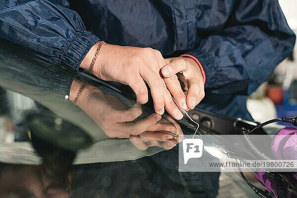 Nahaufnahme Autoglaser bei der Reparatur einer Windschutzscheibe eines Autos in einer Werkstatt. Glas für die Reparatur bohren