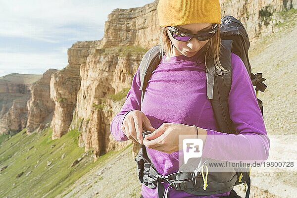 Ein Tourist mit Sonnenbrille setzt einen Rucksack in der Natur auf dem Hintergrund der epischen Felsen Vorbereitung für Trekking mit Klettern. Das Mädchen Wanderer befestigt die Verschlüsse auf dem Rucksack