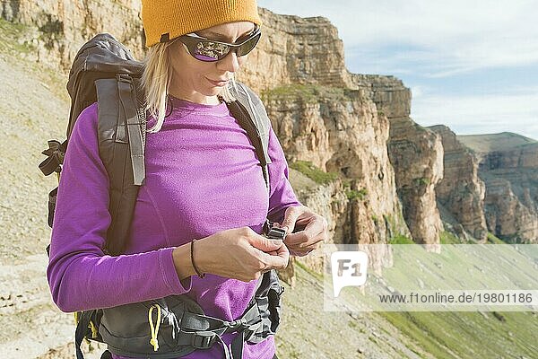 Ein Tourist mit Sonnenbrille setzt einen Rucksack in der Natur auf dem Hintergrund der epischen Felsen Vorbereitung für Trekking mit Klettern. Das Mädchen Wanderer befestigt die Verschlüsse auf dem Rucksack
