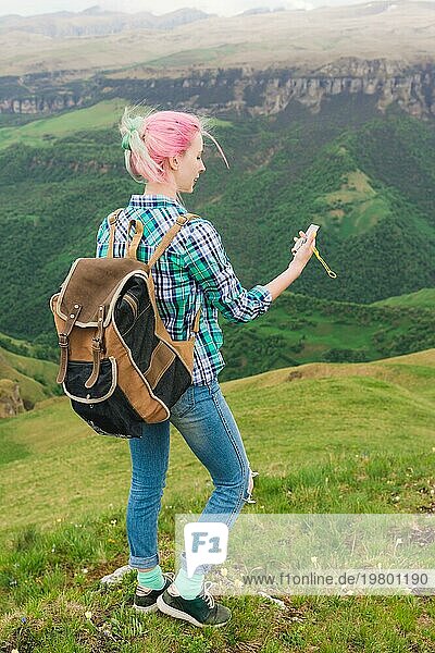 Ein Hipster Mädchen  das von einem Blogger in einem karierten Hemd und mit bunten Haaren mit einem Kompass auf einer Hochebene in den Bergen steht