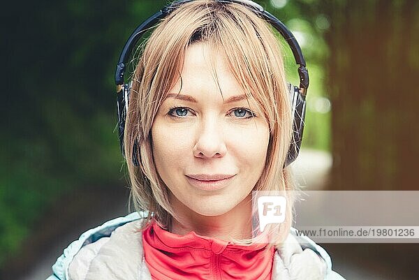 Attraktive blonde Frau im Wald. Nahaufnahme eines sportlichen lächelnden Mädchens beim Musikhören