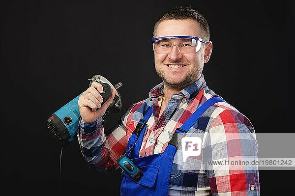 Porträt eines kaukasischen männlichen Mechanikers in Arbeitsuniform mit einer elektrischen Stichsäge um den Hals. Atelierporträt eines handwerklichen Geschäftsmannes