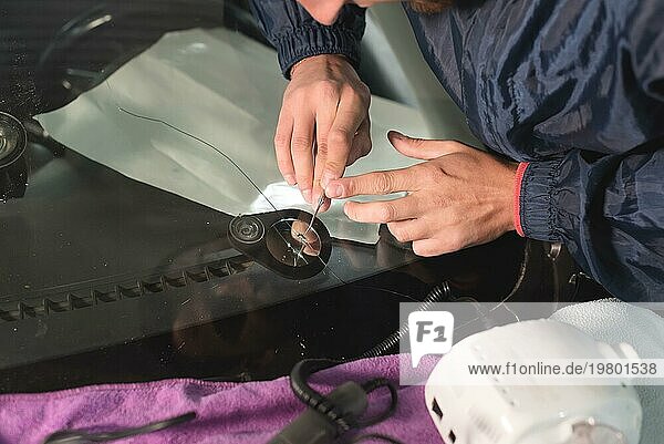 Nahaufnahme Autoglaser bei der Reparatur einer Windschutzscheibe eines Autos in einer Werkstatt. Glas für die Reparatur bohren