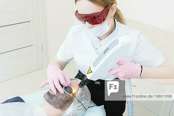 Die Kosmetikerin mit Schutzbrille führt das Verfahren des Carbon Peelings mit Hilfe eines kosmetologischen Lasers durch. Carbon Gesichtspeeling Verfahren. Die Laserimpulse reinigen die Gesichtshaut. Hardware Kosmetologie Behandlung. Prozess der Photothermolyse  Erwärmung der Haut