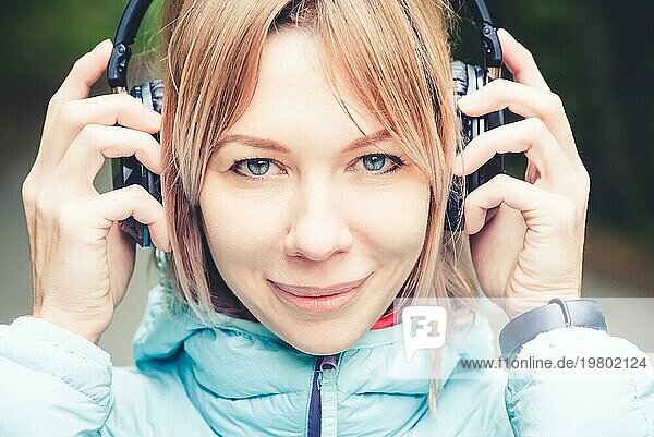 Nahaufnahme Porträt einer schönen jungen Frau mit Kopfhörern  die draußen im Wald Musik hört. Fröhliche Musik