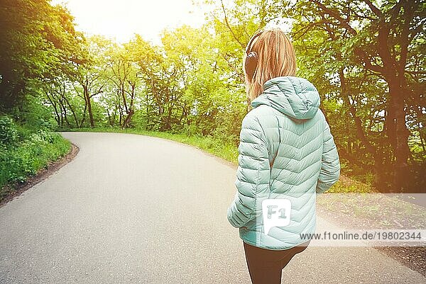Porträt eines attraktiven  sportlichen  blonden Mädchens  das auf einem Waldweg von hinten nach unten läuft und Bluetooth Kopfhörer mit Musik oder Naturgeräuschen trägt