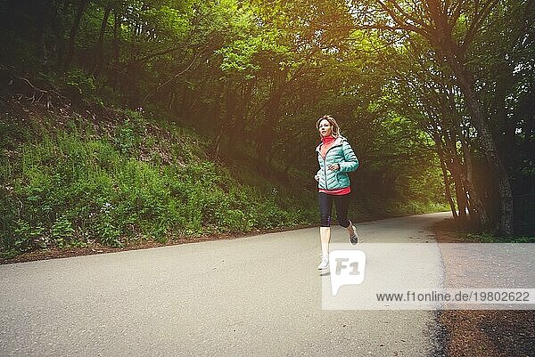 Junge Fitness blonde Frau mit Kopfhörern laufen am Morgen kaukasischen Waldweg in der Sonne Licht
