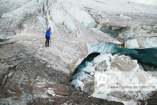 Der Reisende mit Mütze und Sonnenbrille sitzt in den verschneiten Bergen auf dem Gletscher. Reisender in einer natürlichen Umgebung
