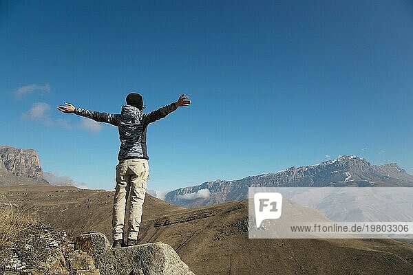 Der Applaus einer jungen Rucksacktouristin auf dem Gipfel eines sich ausbreitenden  ansteigenden Berges. Freiheit und Sieg vor dem Hintergrund von Bergen und blauem Himmel