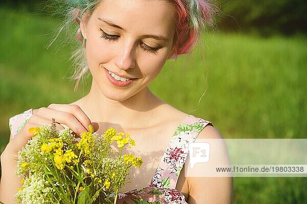 Porträt eines jungen  glücklich lächelnden Mädchens in einem Baumwollkleid mit einem Strauß Wildblumen