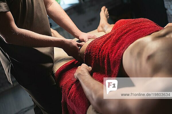 Männliche professionelle Sportmassage der Hüfte und des Knies in einem dunklen Massageraum. hochwertige Massagedienstleistungen. Kopierraum