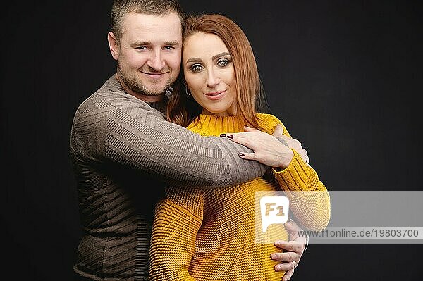 Porträt eines attraktiven kaukasischen Ehepaares  Mann und Frau  die sich auf schwarzem Hintergrund umarmen. Glückliche Familienbeziehungen