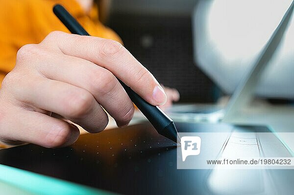 Lässiger Mann  Freiberufler mit Stift  schreibt auf digitalem Tablet Bildschirm  arbeitet an Laptopcomputer im Büro Schreibtisch. Grafik oder Webdesigner bei der Arbeit an seinem Web Design Projekt  Nahaufnahme