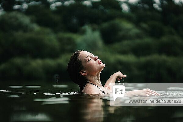 Ein junges  schlankes  schönes und heißes Mädchen mit nassen Haaren und großen Lippen schwimmt im See  reist zu Wasserfällen  entspannt sich am See