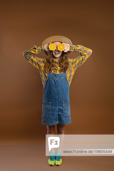 Studioporträt einer fröhlichen Hipster Frau  die ein komisches Gesicht macht und ihre Augen mit Orangen bedeckt