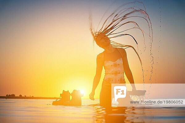 Silhouette einer schlanken jungen Athletin Kitesurfer schwimmt bei Sonnenuntergang im Meer neben ihrem Kite Board