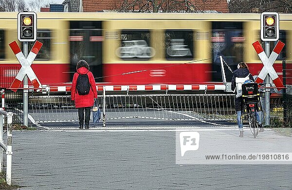 Zwei Frauen warten an einerm beschrankten Bahnübergang während der Durchfahrt eines S- Bahn Zugs  Berlin  10.01.2023