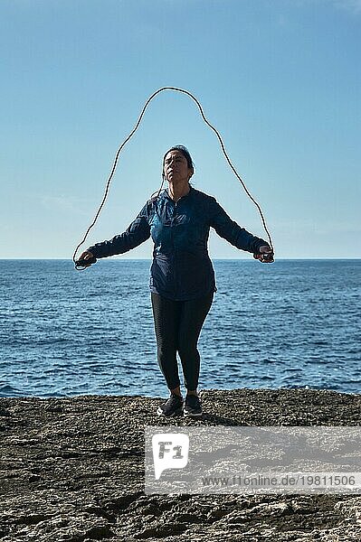 Lateinamerikanische Frau  mittleres Alter  trägt Sportkleidung  Training  macht körperliche Übungen  Planke  Sit ups  Kletterschritt  verbrennt Kalorien  hält sich fit  draußen am Meer  trägt Kopfhörer  Smartwatch