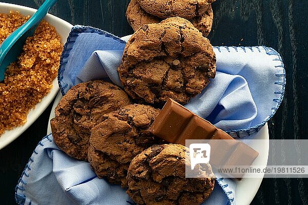 Chocolate Chip Cookies auf einem weißen Teller neben braunem Zucker und ein Stück Milchschokolade  Draufsicht Schokoladenkekse. Auflösung und hohe Qualität schönes Foto
