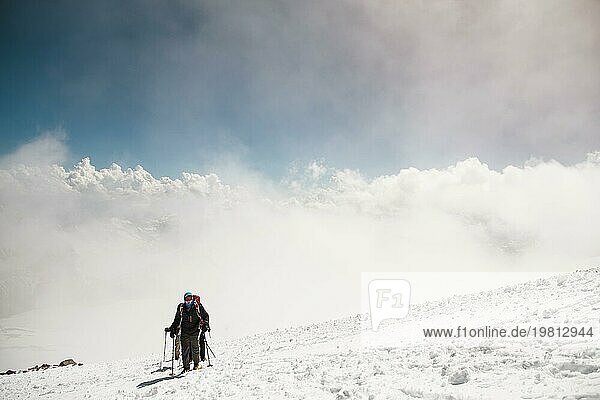 Eine Gruppe von Bergsteigern erklimmt den Gipfel eines schneebedeckten kaukasischen Berges vor der Kulisse der felsigen  schneebedeckten Bergspitzen