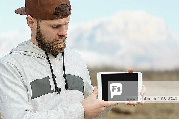 Nahaufnahme Porträt eines Hipsters mit einer braunen Mütze im Freien  der ein weißes Tablet PC in den Händen hält. Ein bärtiger Mann schaut auf das Tablet. Hintergrund unscharf
