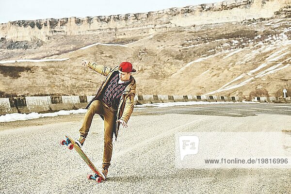 Stylish happy Junger Mann in Mütze und Hose Jogger rollen auf einem Longboard eine Bergstraße hinunter  genießen das Leben