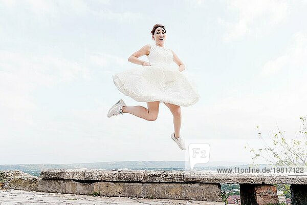 Die verrückte Braut springt und hängt in der Luft vor der Kulisse der Stadtlandschaft eines kleinen Ferienortes im Nordkaukasus. Das Konzept von Spaß und Wahnsinn bei der Hochzeit