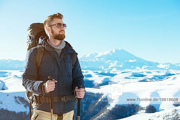 Ein Hipster Reisender mit Bart und Sonnenbrille in der Natur. Ein Mann wandern in den Bergen mit einem Rucksack und skandinavischen Wanderstöcke im Hintergrund eines Berges Elbrus Landschaft und blaün Himmel. Reisen Lifestyle Abenteuer Outdoor Erholung übertreffen