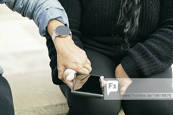 Zwei spanisch lateinamerikanische Frauen mit Smartphones und Smartwatches  selektiver Fokus auf die abgeschnittenen Hände. technologisches Konzept von Kommunikation und Freiheit