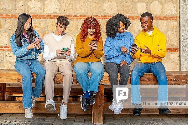 Frontalansicht einer Gruppe multiethnischer junger Freunde  die auf einer Bank in der Stadt sitzen und telefonieren