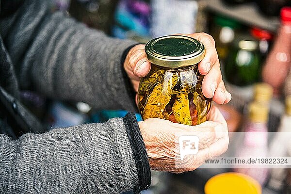 Alte faltige Hände halten ein Glas mit Bergmarmelade aus den Blättern der kaukasischen Bäume in den Bergen