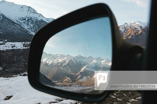 Reflexion einer schönen Berglandschaft bei Sonnenuntergang im Seitenspiegel der Rückansicht. Das Konzept des Reisens mit dem Auto. Kaukasusgebirge in Oberbalkarien
