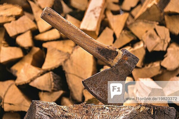 Die Axt steckt in einem Baumstamm vor dem Hintergrund von gehacktem Brennholz  das auf einem flachen Stapel liegt. Nahaufnahme