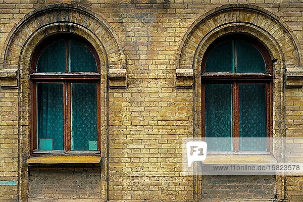 Zwei Vintage Bogenfenster in einer Wand aus gelben Ziegeln. Grün  die Farben der Meereswelle Glas in einem kastanienbraunen dunkelroten Holzrahmen. Das Konzept der antiken Vintage Architektur in Gebäudeelemente
