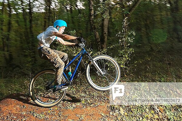 Ein junger Radfahrer mit Helm landet nach einem Sprung von einem hohen Kicker auf einem Waldradweg auf dem Fahrrad. Schießen mit langer Belichtung Verdrahtung