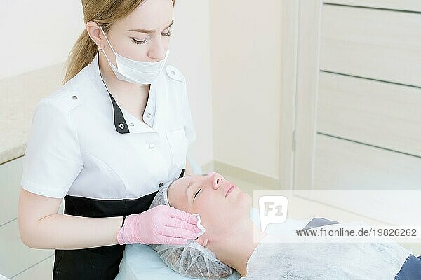Reinigungsverfahren im Büro der Kosmetologie. Kosmetikerin in rosa Handschuhe sind aus dem Gesicht eines jungen Mädchens mit einem Schwamm Reinigung der Maske entfernt