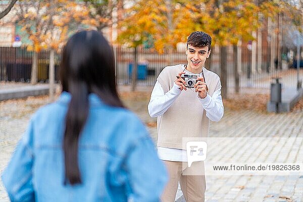 Junger Mann  der ein Foto mit einer Digitalkamera für einen Freund in der Stadt macht