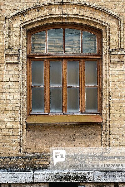 Vintage gewölbtes Fenster in der Wand aus gelbem Backstein. Schwarzes Glas in einem kastanienbraunen dunkelroten Holzrahmen. Das Konzept der antiken Vintage Architektur in Gebäudeelemente