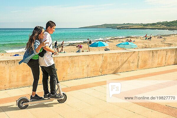 Ein Paar auf einem Motorroller genießt einen sonnigen Tag am Strand mit Menschen und dem Meer in der Ferne