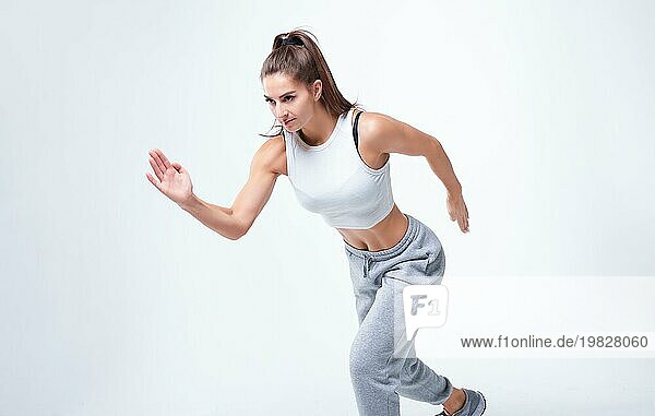 Sportliche Läuferin auf weißem Hintergrund. Foto einer attraktiven Frau in modischer Sportkleidung. Dynamische Bewegung. Seitenansicht. Sport und gesunder Lebensstil. Gemischte Medien