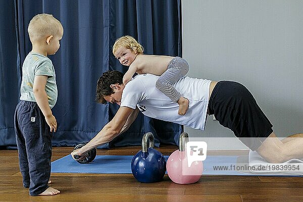 Topic: Young man with a child on his back trains with an abdominal trainer