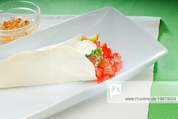 Frischer traditioneller Falafel Wrap auf Fladenbrot mit frischen gehackten Tomaten  Foodfotografie