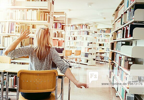 Müde Studentin sitzt am Schreibtisch mit Stapel von Büchern  Universitätsbibliothek