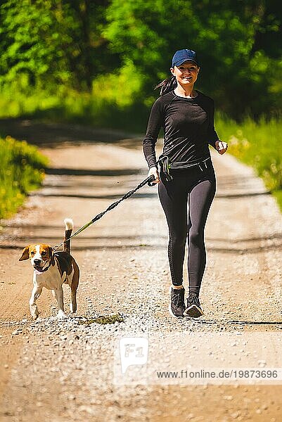 Sportliches Mädchen läuft mit einem Hund (Beagle) an einem sonnigen Frühlingstag auf einem Waldweg. Raum in der Natur kopieren