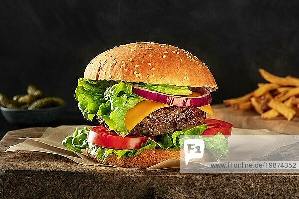 Burger mit Rindfleisch  Käse  Zwiebel  Tomate und grünem Salat  eine Seitenansicht auf einem dunklen Hintergrund mit Essiggurken und Pommes frites