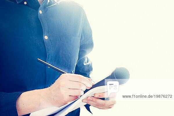Ausschnitt eines männlichen Journalisten in einem blaün Hemd bei einer Pressekonferenz  der Notizen macht und ein Mikrofon hält