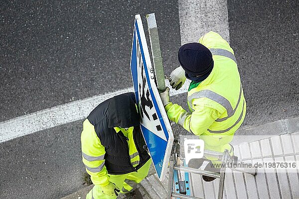 Arbeiter wechseln ein beschädigtes Straßenschild auf dem Gehweg aus. Öffentliches Instandhaltungskonzept