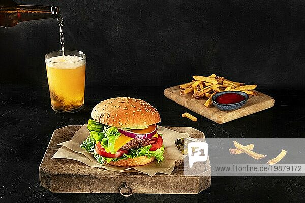 Burger und Bier. Hamburger mit Rindfleisch  Käse  Zwiebel  Tomate und grünem Salat  auf dunklem Hintergrund mit Kopierraum  Essiggurken und Pommes frites. Selektiver Fokus