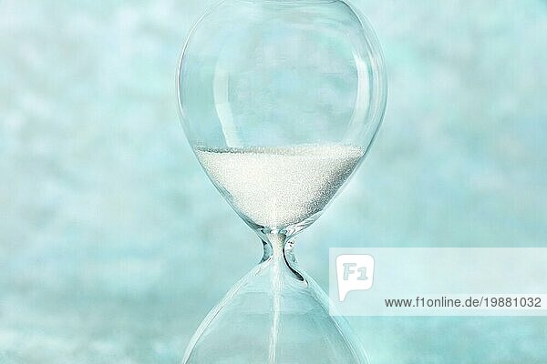 Die Zeit läuft ab Konzept. Eine Nahaufnahme einer Sanduhr  durch die Sand fällt  auf einem blaugrünen Hintergrund mit Platz für Text