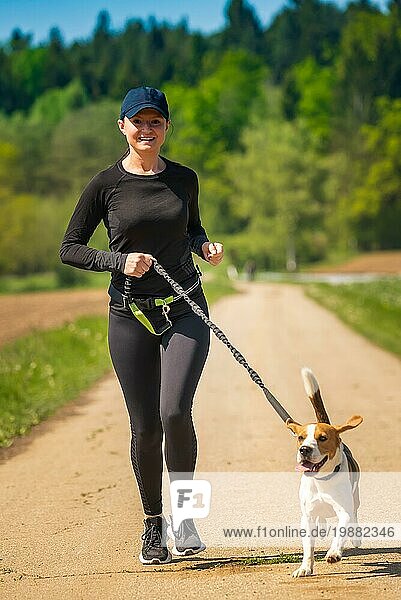 Sportliches Mädchen läuft mit einem Hund (Beagle) an einem sonnigen Frühlingstag auf einem Waldweg. Raum in der Natur kopieren